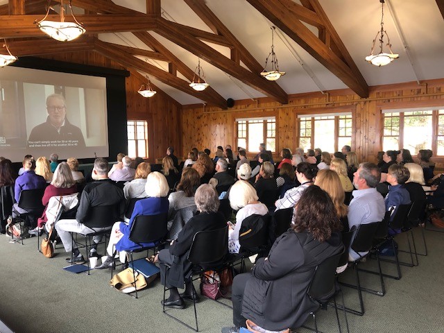 Auditorium full of people watching an educational program on a screen about elderly care